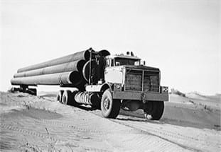 Old photo of Kenworth truck transporting large pipes on construction site